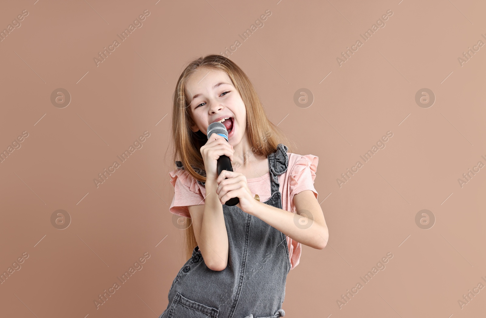 Photo of Little girl with microphone singing on light brown background