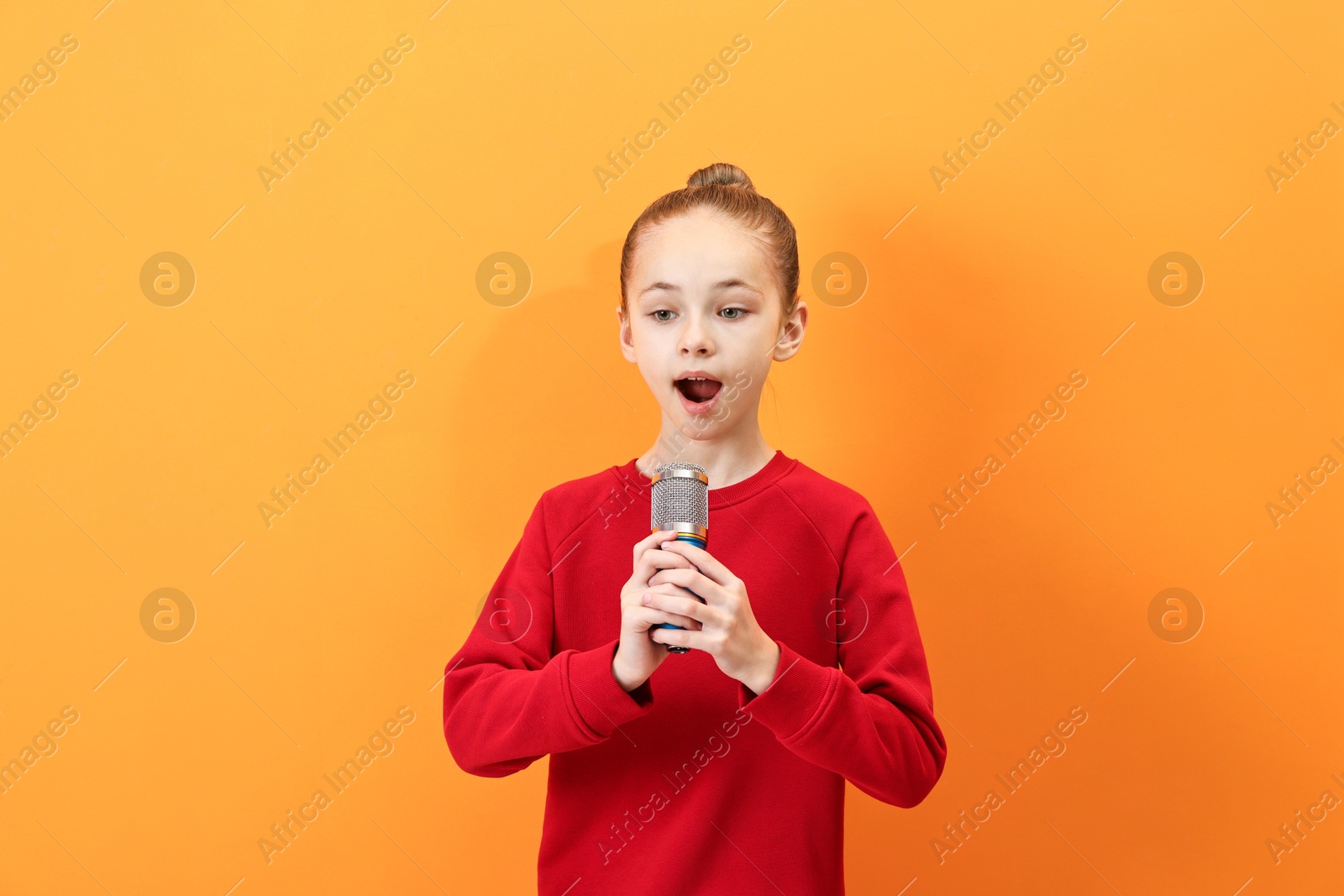 Photo of Little girl with microphone singing on orange background