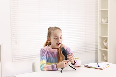 Photo of Little girl with microphone at white table indoors