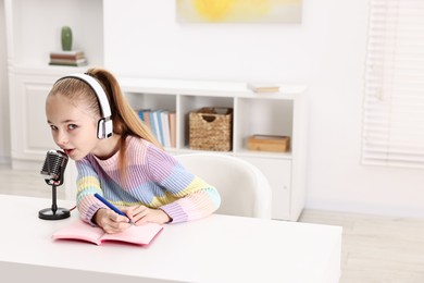 Photo of Little girl with microphone and headphones at white table indoors, space for text