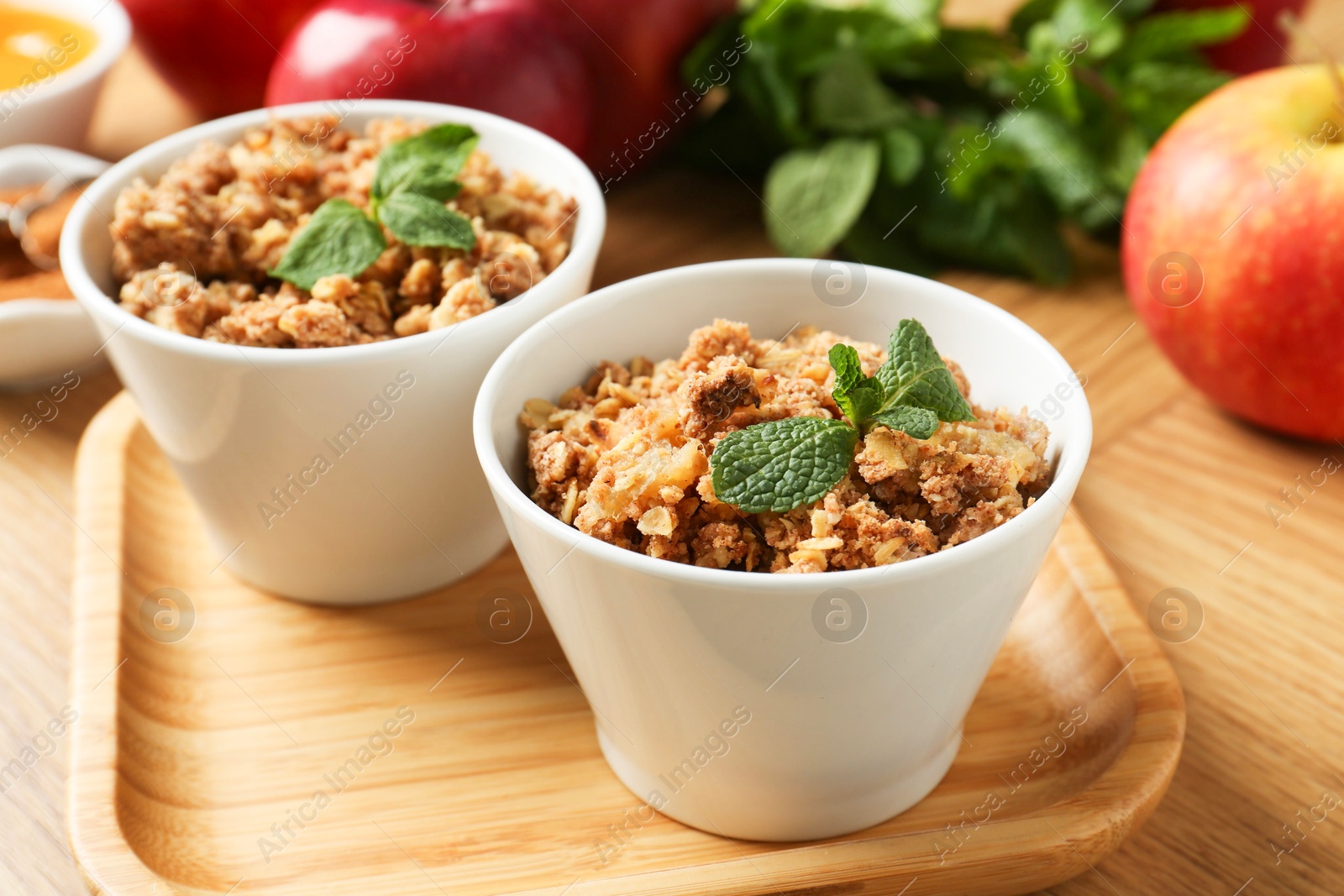 Photo of Delicious apple crisp with mint in bowls on wooden table, closeup