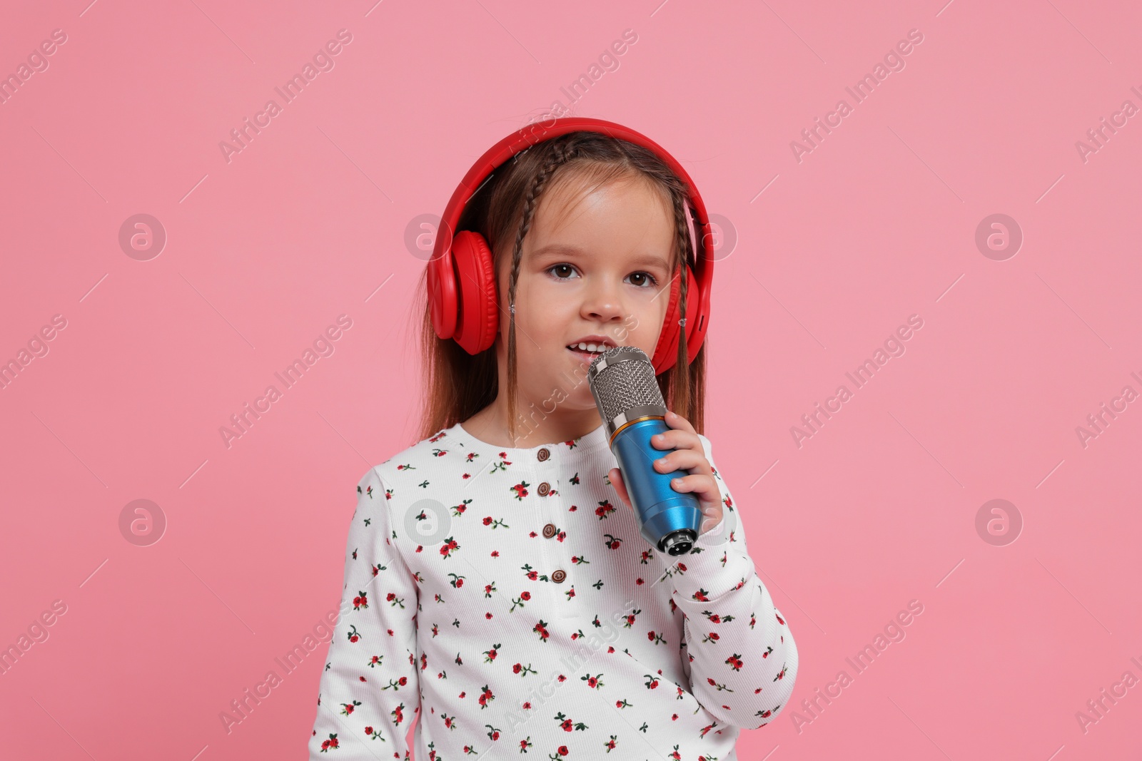 Photo of Cute girl with microphone and headphones singing on pink background