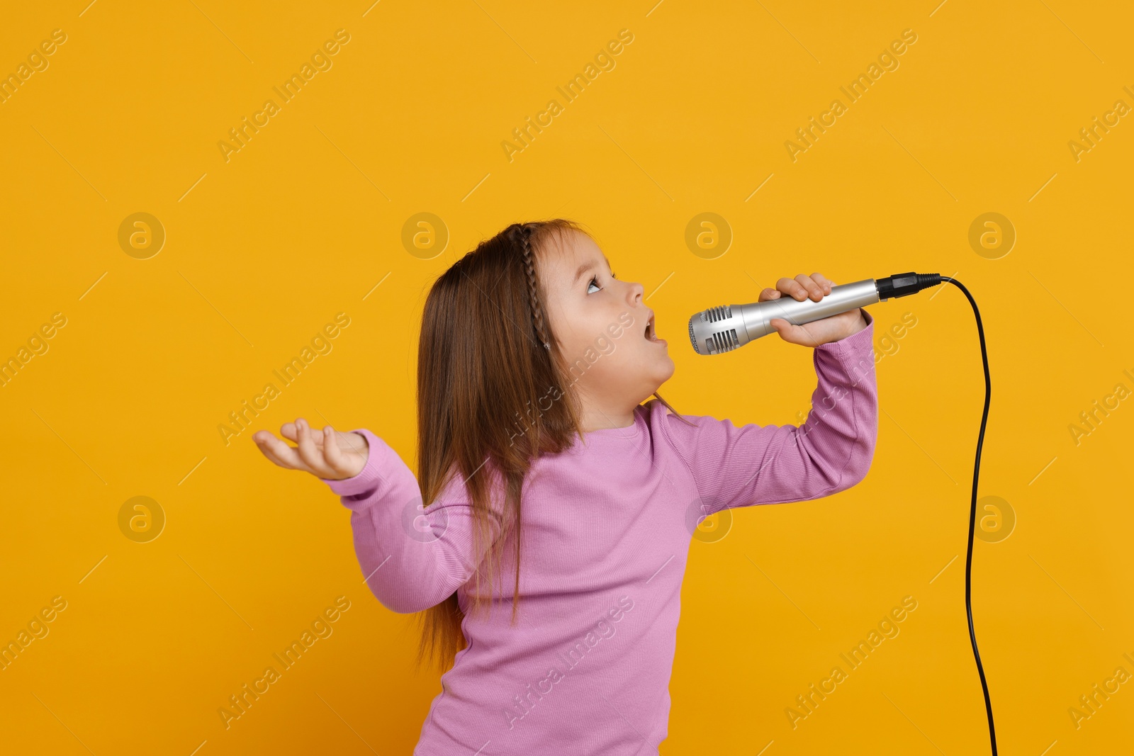 Photo of Cute girl with microphone singing on orange background