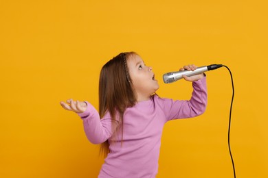 Photo of Cute girl with microphone singing on orange background