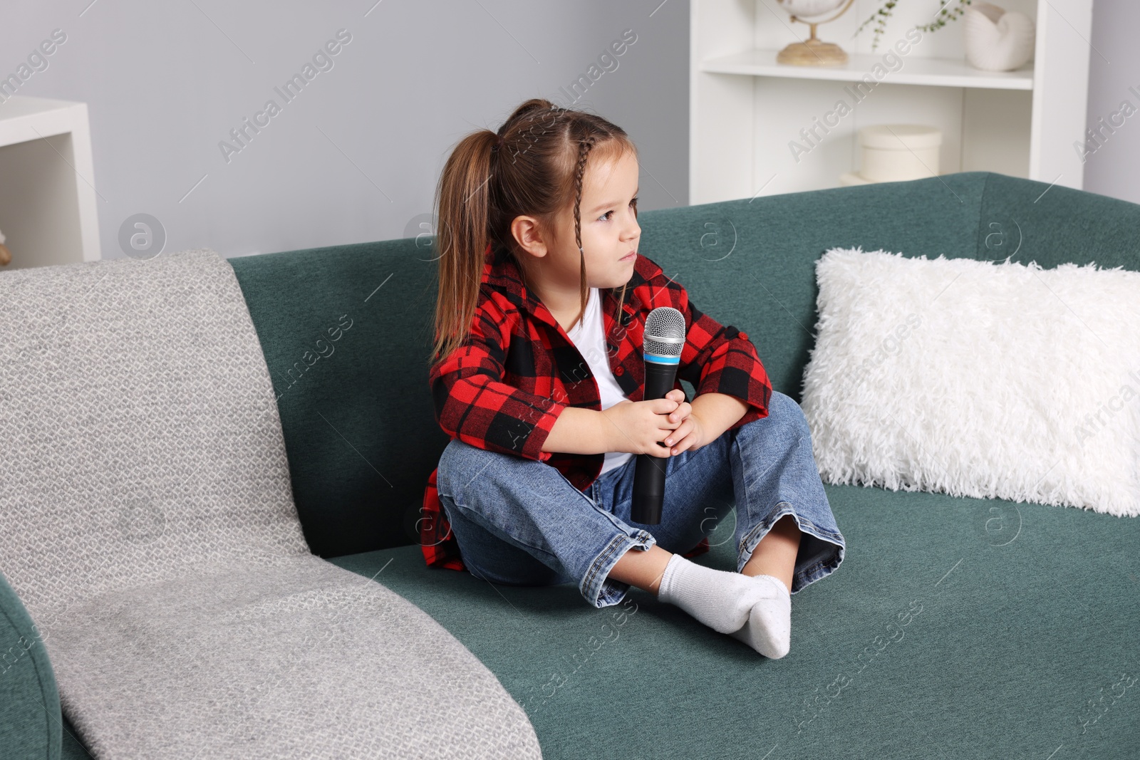 Photo of Cute girl with microphone sitting on sofa at home