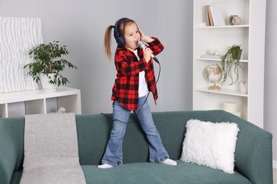 Photo of Cute girl with microphone in headphones singing on sofa at home