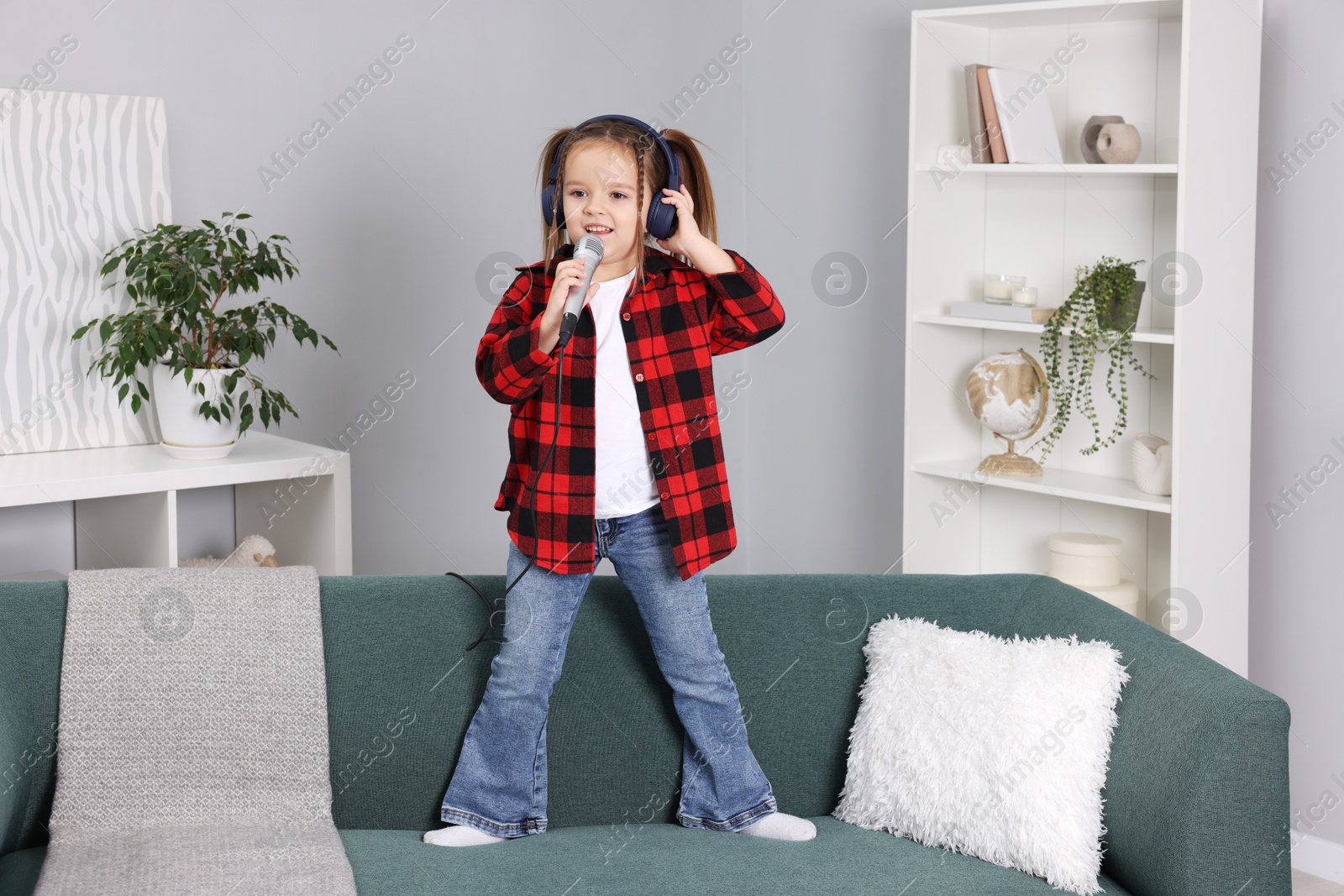 Photo of Cute girl with microphone in headphones singing on sofa at home