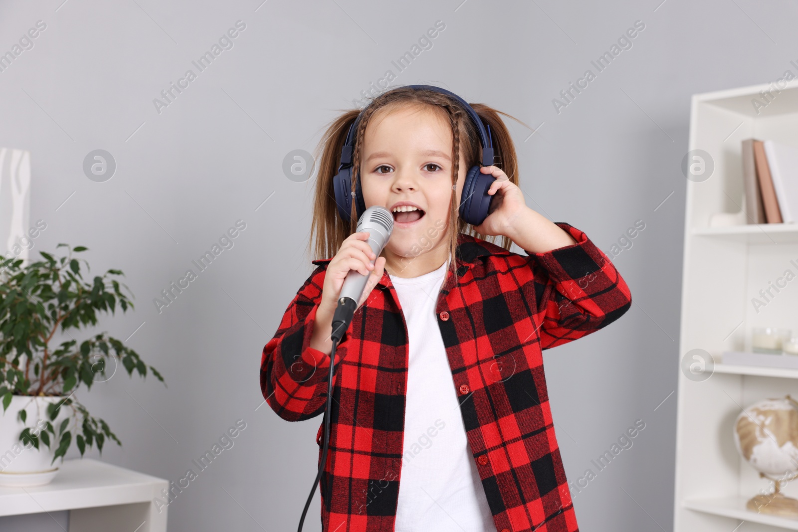 Photo of Cute girl with microphone in headphones singing at home