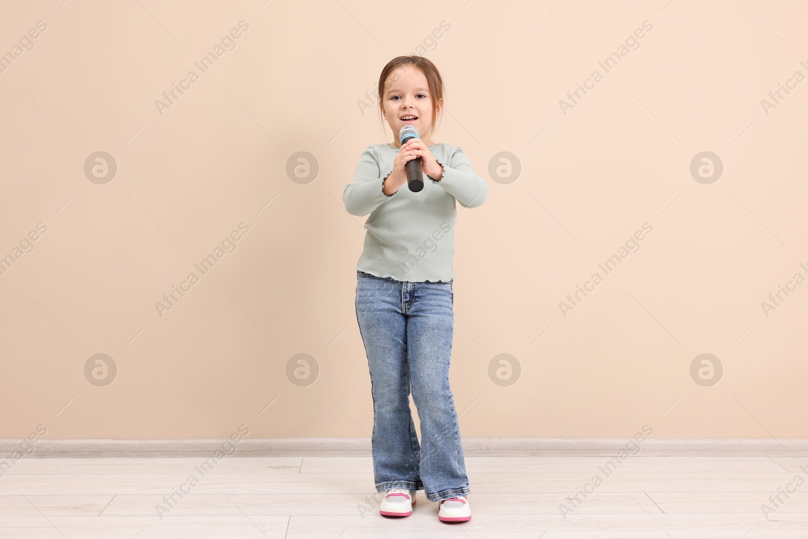 Photo of Cute girl with microphone singing near beige wall