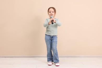 Photo of Cute girl with microphone singing near beige wall