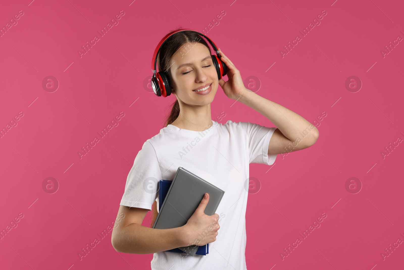 Photo of Portrait of smiling teenage girl in headphones with books on pink background