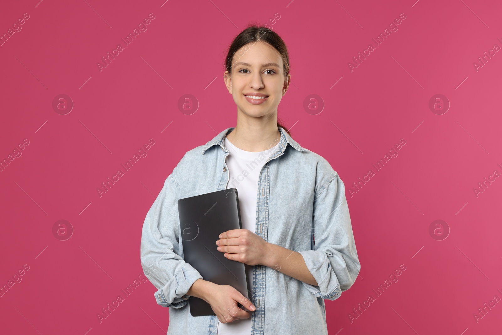 Photo of Portrait of smiling teenage girl with laptop on pink background