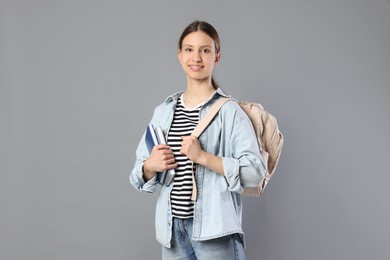 Photo of Portrait of smiling teenage girl with books and backpack on grey background