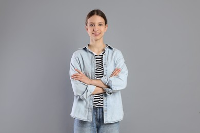 Photo of Portrait of smiling teenage girl with crossed arms on grey background