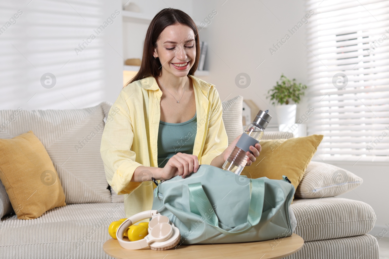 Photo of Happy woman packing her gym bag on sofa at home