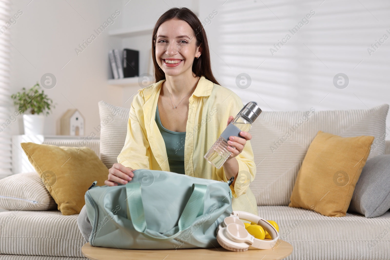 Photo of Happy woman packing her gym bag on sofa at home