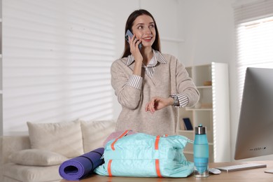 Photo of Happy woman talking on phone while packing gym bag at desk indoors