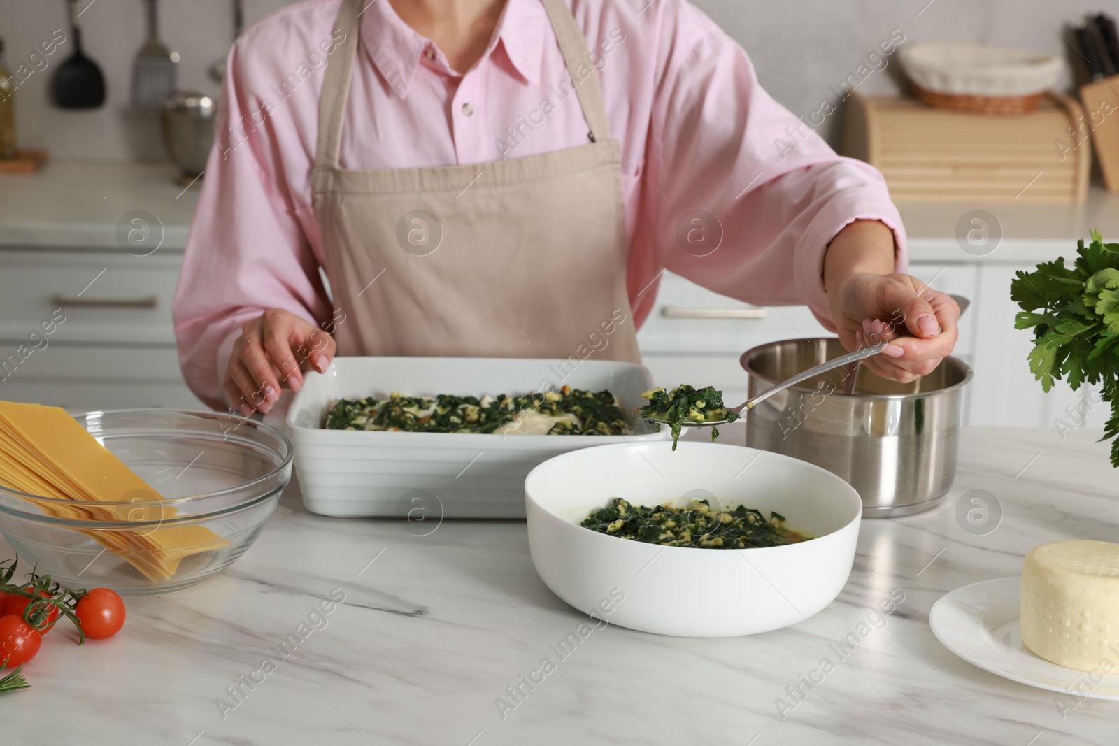 Photo of Woman making spinach lasagna at marble table in kitchen, closeup