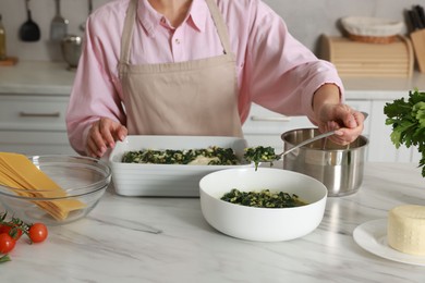 Photo of Woman making spinach lasagna at marble table in kitchen, closeup