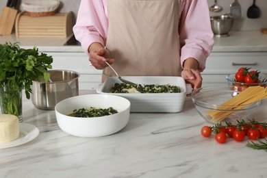 Photo of Woman making spinach lasagna at marble table in kitchen, closeup