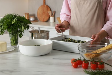 Photo of Woman making spinach lasagna at marble table in kitchen, closeup