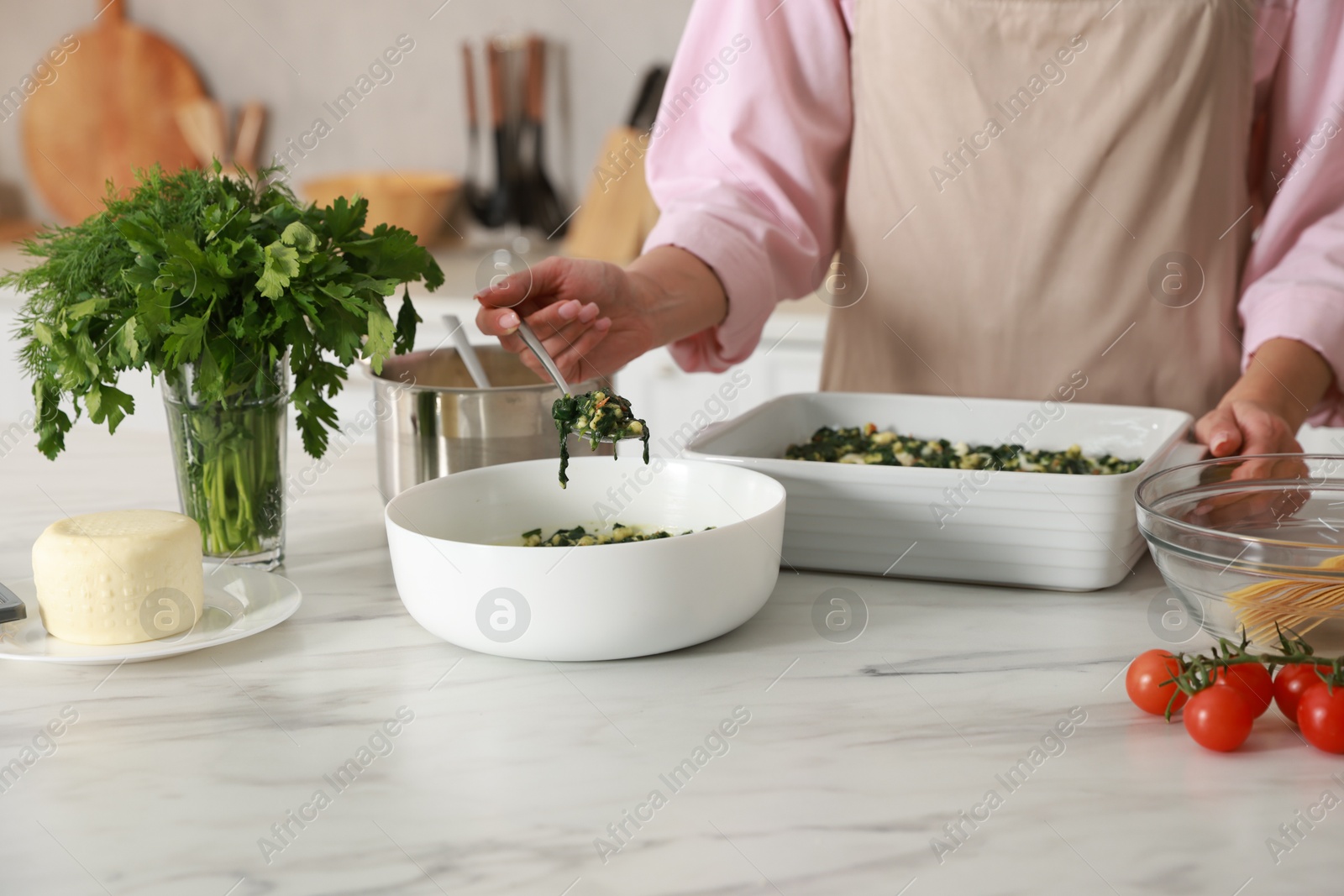 Photo of Woman making spinach lasagna at marble table in kitchen, closeup