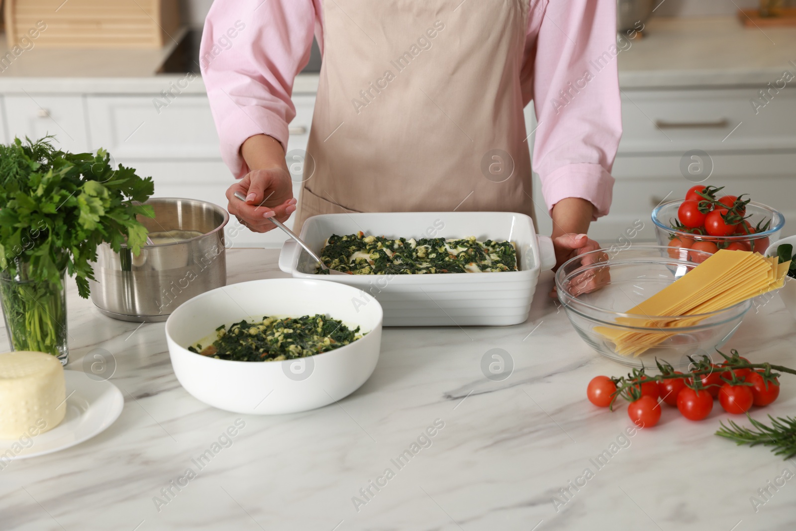 Photo of Woman making spinach lasagna at marble table indoors, closeup