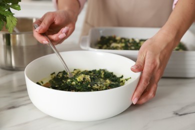 Photo of Woman making spinach lasagna at marble table indoors, closeup