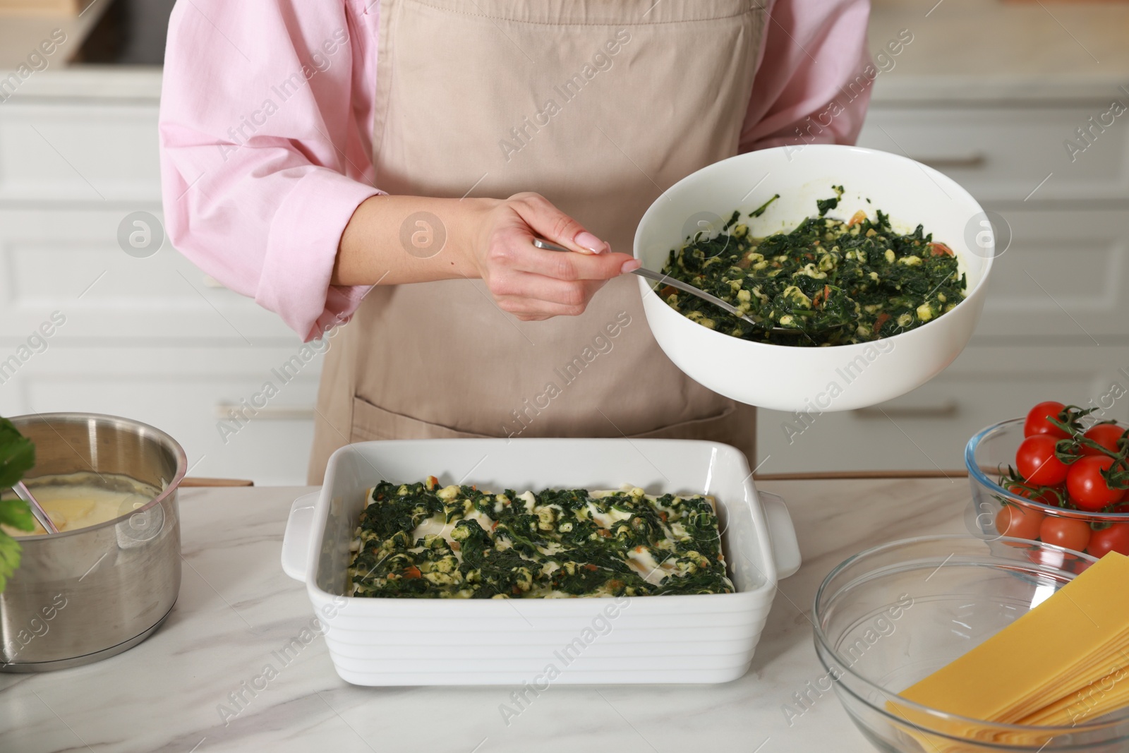 Photo of Woman making spinach lasagna at marble table indoors, closeup