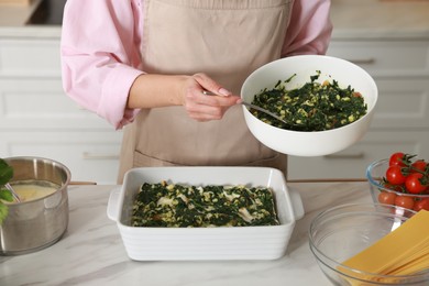 Photo of Woman making spinach lasagna at marble table indoors, closeup