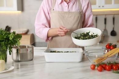 Photo of Woman making spinach lasagna at marble table in kitchen, closeup