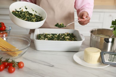 Woman making spinach lasagna at marble table indoors, closeup