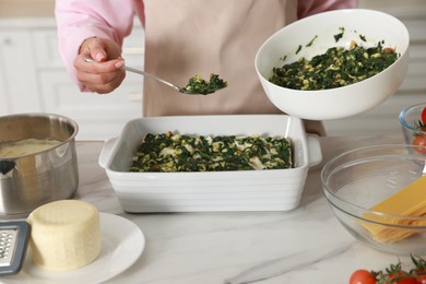 Photo of Woman making spinach lasagna at marble table indoors, closeup