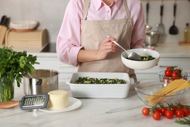 Photo of Woman making spinach lasagna at marble table in kitchen, closeup