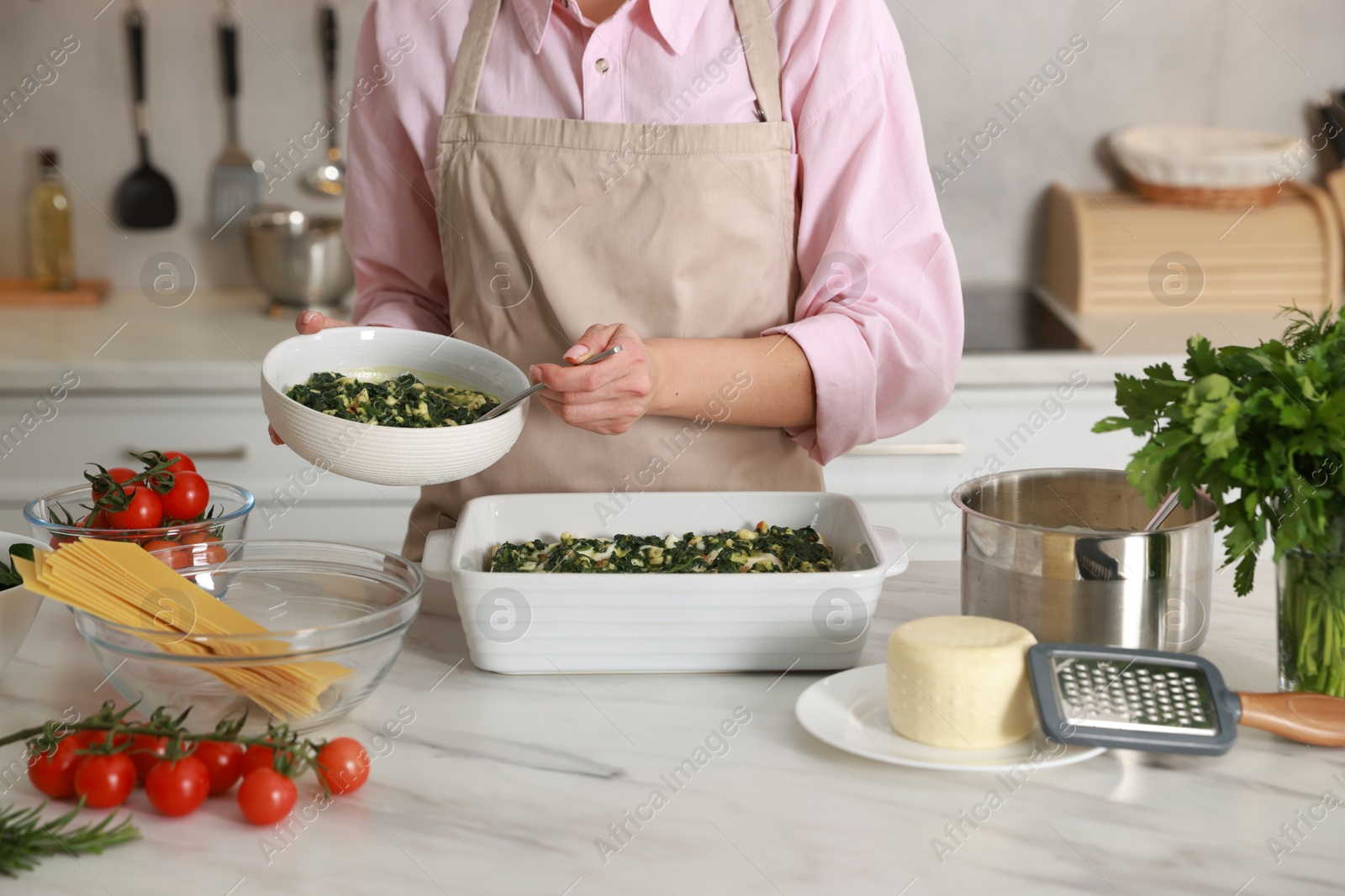 Photo of Woman making spinach lasagna at marble table in kitchen, closeup