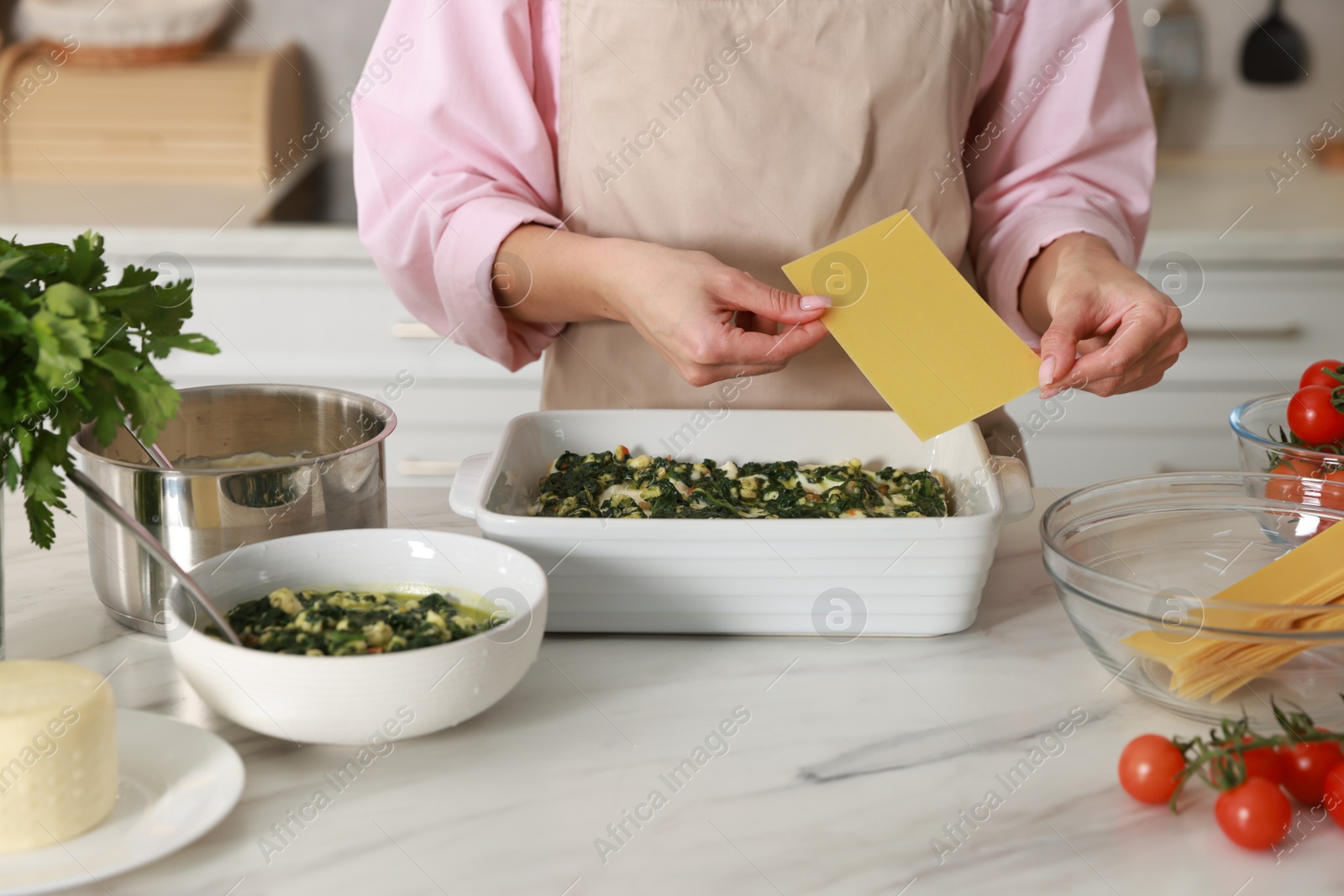 Photo of Woman making spinach lasagna at marble table indoors, closeup