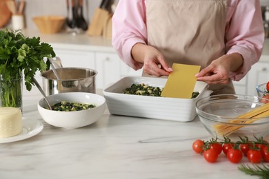 Photo of Woman making spinach lasagna at marble table indoors, closeup