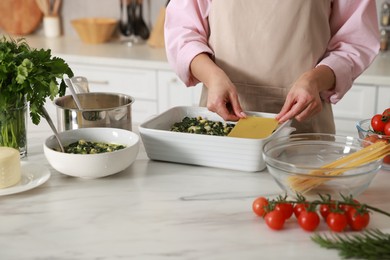 Photo of Woman making spinach lasagna at marble table indoors, closeup