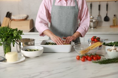 Photo of Woman making spinach lasagna at marble table in kitchen, closeup