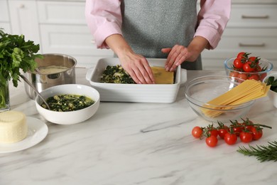 Photo of Woman making spinach lasagna at marble table indoors, closeup