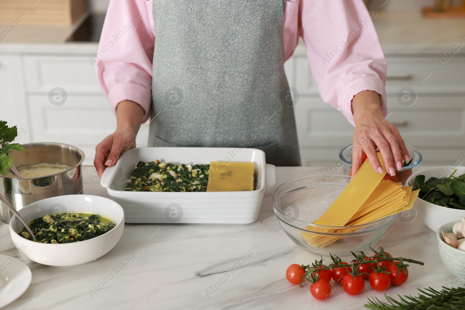 Photo of Woman making spinach lasagna at marble table indoors, closeup