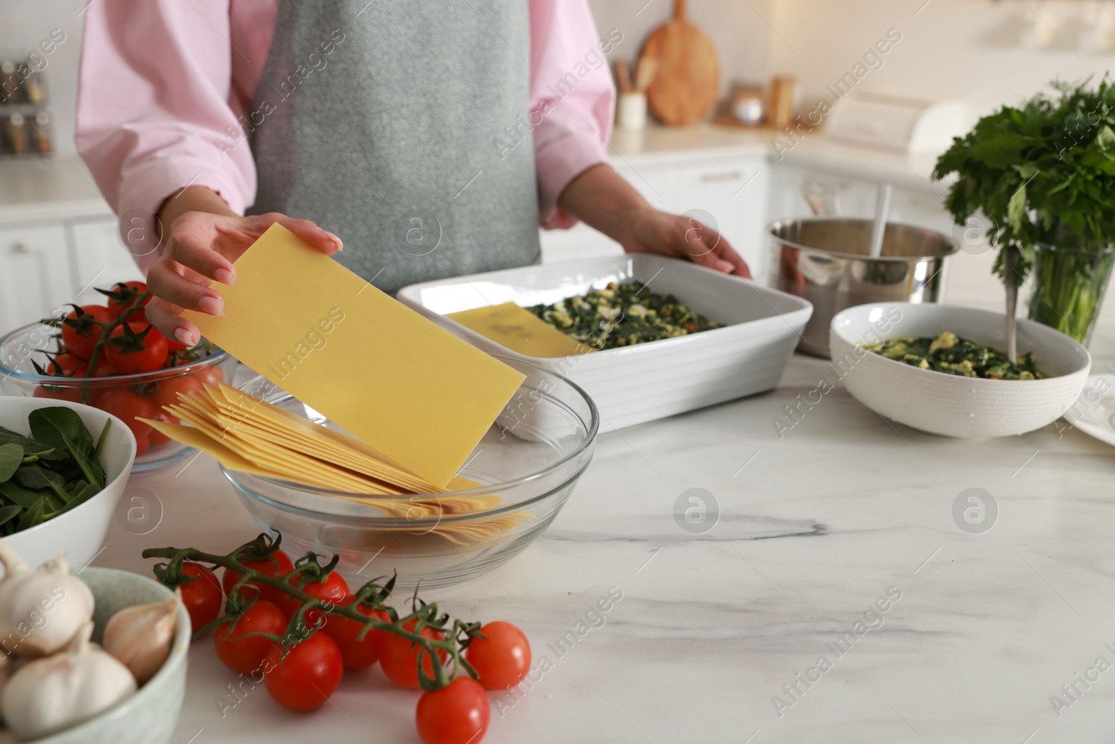 Photo of Woman making spinach lasagna at marble table indoors, closeup