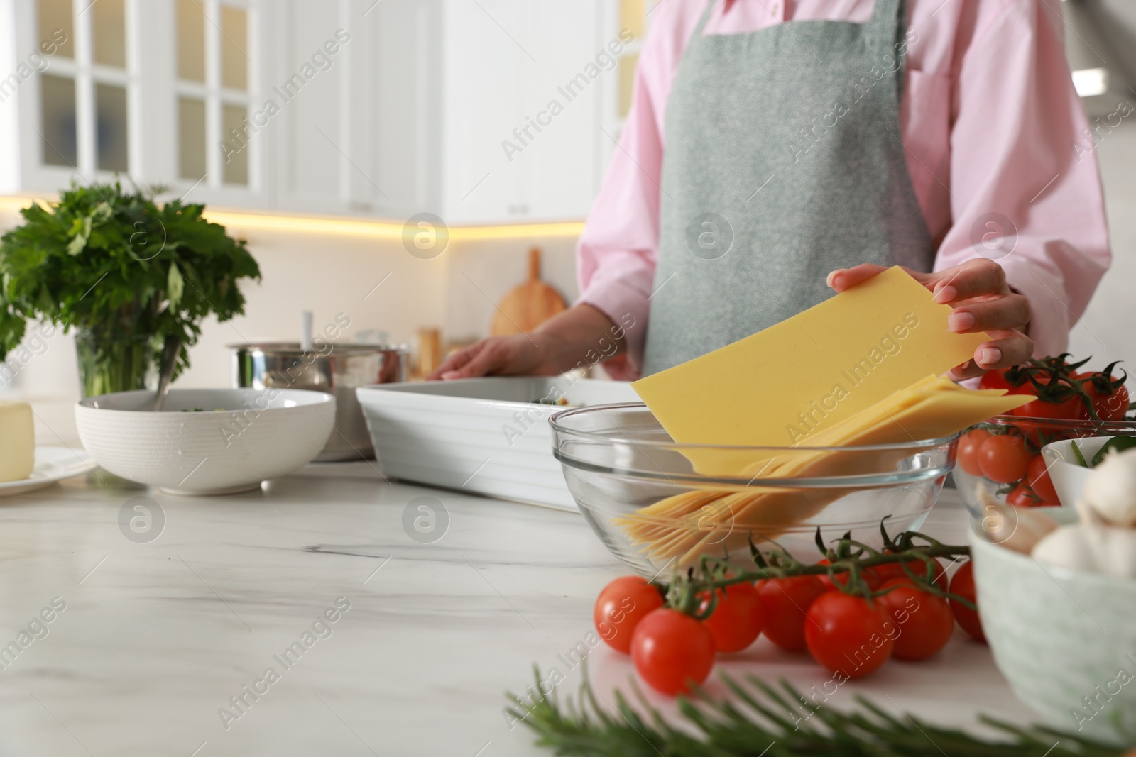 Photo of Woman making spinach lasagna at marble table indoors, closeup