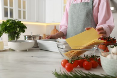 Photo of Woman making spinach lasagna at marble table indoors, closeup