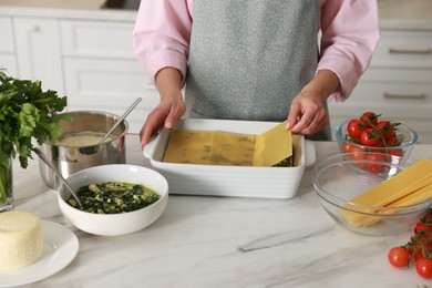 Photo of Woman making spinach lasagna at marble table indoors, closeup