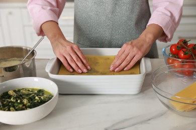 Photo of Woman making spinach lasagna at marble table indoors, closeup