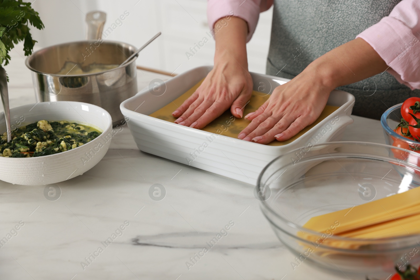 Photo of Woman making spinach lasagna at marble table indoors, closeup