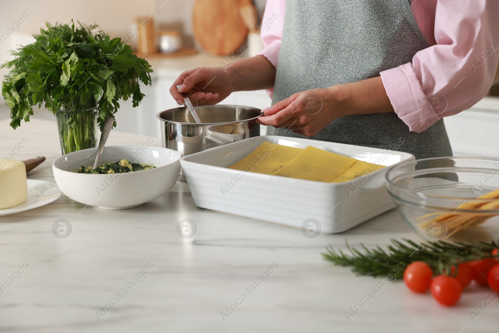 Photo of Woman making spinach lasagna at marble table indoors, closeup