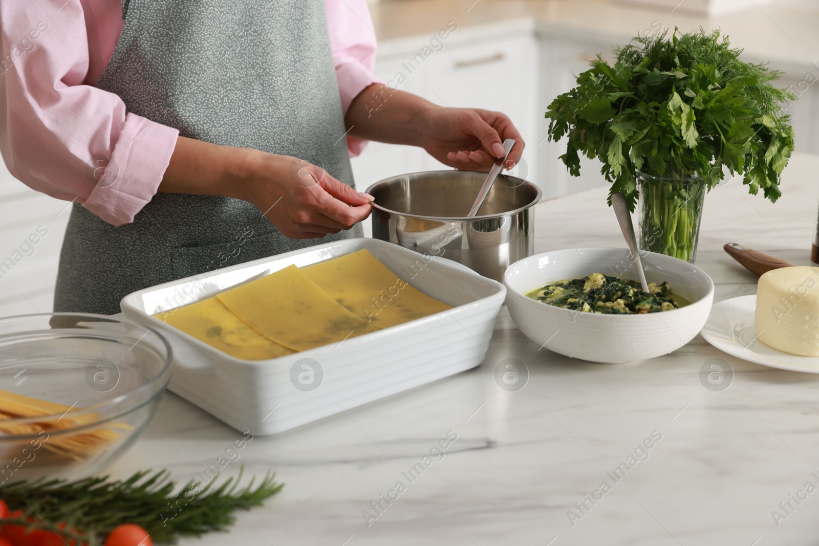 Photo of Woman making spinach lasagna at marble table indoors, closeup