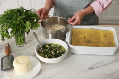 Photo of Woman making spinach lasagna at marble table indoors, closeup